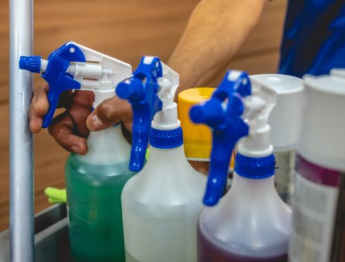 hand of young janitorial worker holding a sprayer with cleaner in trolley of cleaning supplies